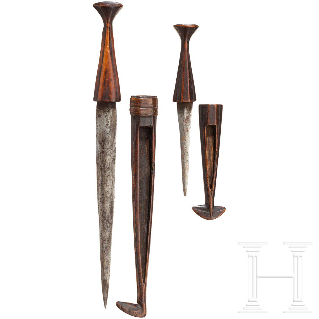 Two knives of the Ovambo, Africa: Jeweils zweischneidige, unterschiedlich lange Eisenklingen mit facettierten Holzgriffen. Die einseitig offenen Holzscheiden jeweils mit fischschwanzfÃ¶rmigem Abschluss am Ort (bei einer unvollstÃ¤