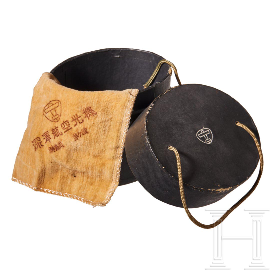 A case for Japanese Flyer Goggles: Oval cardboard case with lid, black ribbed paper covering, embossed silver makerâ€™s mark on lid, secured to base by brown knotted thread. Includes small yellow lens-cleaning cloth with makerâ��