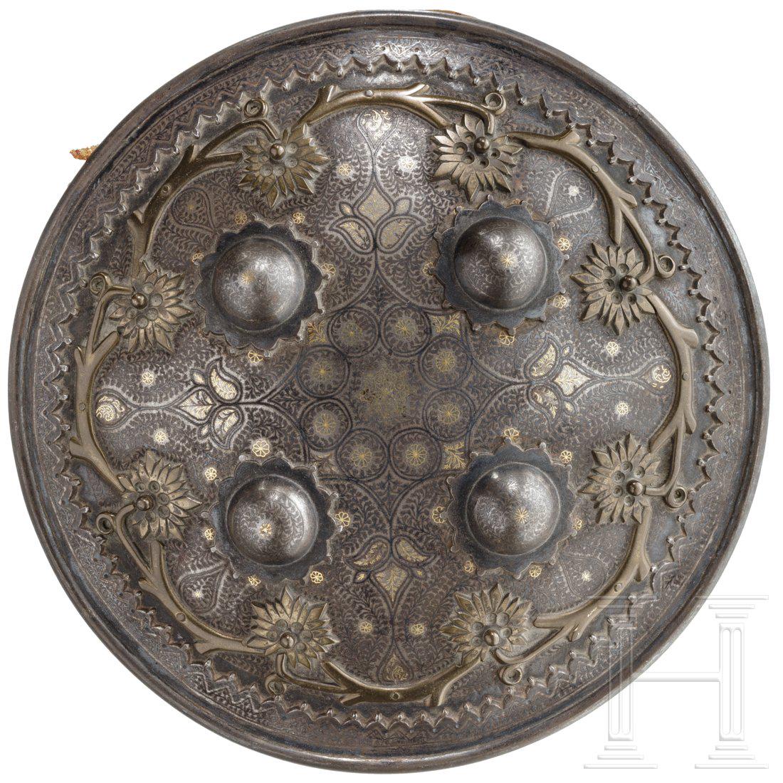An Indian buckler, Lahore, 19th century: An Indian buckler, Lahore, 19th century Leicht gewÃ¶lbter Schild mit reicher Silber- und Messingtausia sowie floralen Messingauflagen und aufgelegtem Rand, vs. vier en suite dekorierte Messingbuckel