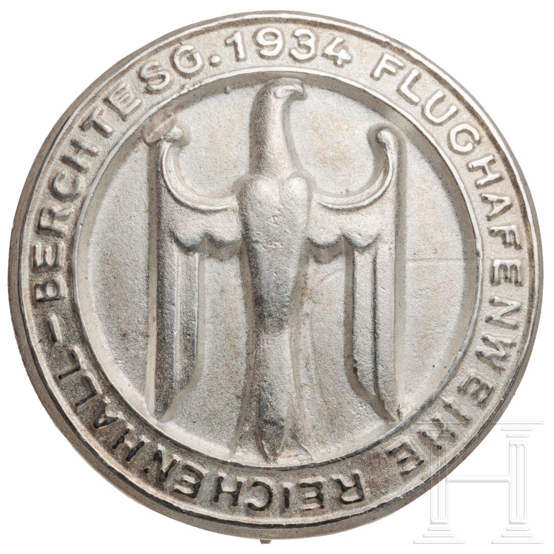 A badge for guests of honour at the opening of the: Rundes silbernes Abzeichen mit polierten Details, darauf ein stilisierter reliefierter Adler in Umschrift "Flughafenweihe Reichenhall-Berchtesg. 1934". RÃ¼ckseitig breite Vertikalnadel, Feingehaltsp