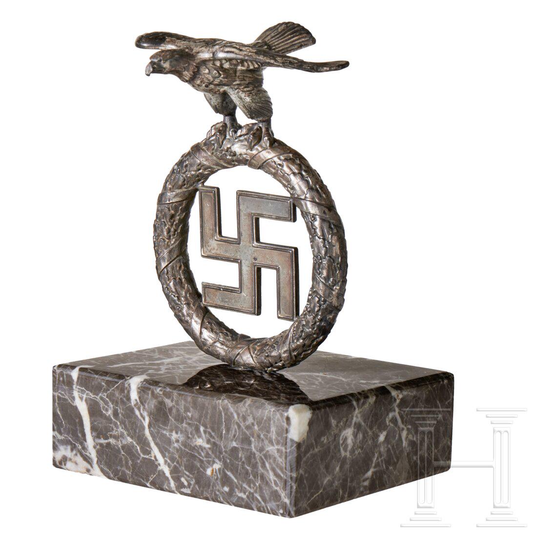 A “Deutschland Erwache” Desk Eagle: A “Deutschland Erwache” Desk Eagle Cast silver finished “Gahr” style eagle and wreathed swastika standard finial, mounted to a grey and white marble base. Size ca. 28 x 19 cm (