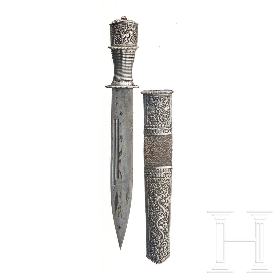 A Tibetan dughti, 19th/20th century: A Tibetan dughti, 19th/20th century Kräftige, spitz zulaufende Keilklinge, beidseitig mit zwei Zügen, Griff mit reliefierter Hilze aus Silber und Drahtwicklung. Scheide ebenfalls silbermonti