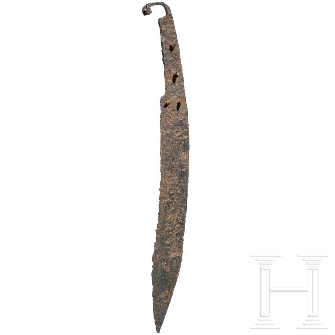 A Greek curved single-edged sword (kopis), 4th - 2nd century B.C.: A Greek curved single-edged sword (kopis), 4th - 2nd century B.C.Single-edged, curved cutlass with a broad blade and a recurved pommel in the shape of a stylised animal head. Four rivets preserved in 