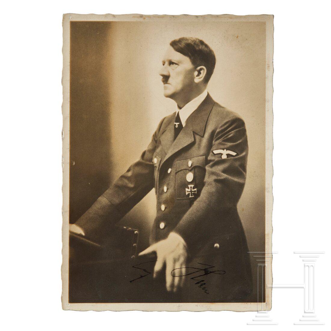 Adolf Hitler - a signed Hoffmann postcard: A Postcard of Adolf HitlerHeinrich Hoffman photograph of Adolf Hitler at podium in wartime field-grey open-collar tunic. Handwritten ink signature on lower center margin. Un-used, glue residue on reve