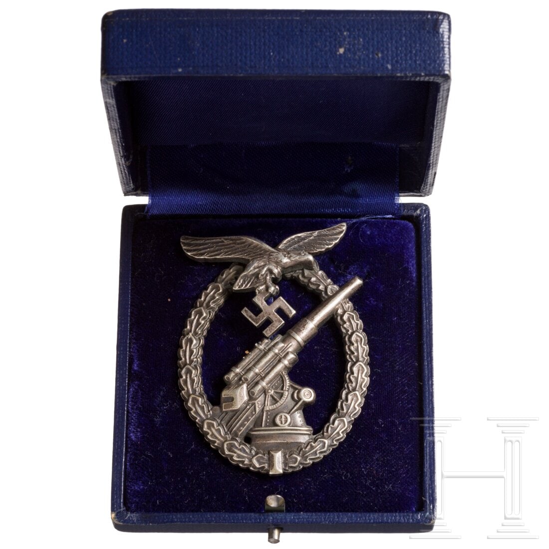 A cased Luftwaffe Flak Artillerie Badge: A cased Luftwaffe Flak Artillerie BadgeVersilberte, dunkel patinierte BuntmetallausfÃ¼hrung mit rs. vertikaler Drahtnadel und Punze "Brehmer Markneukirchen". Blaues Etui mit Goldaufdruck und blauem 