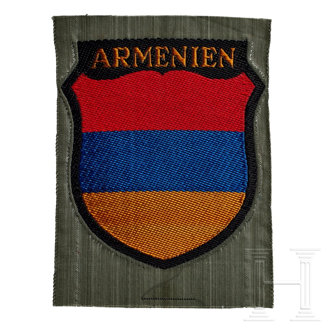 An Arm Shield for Armenian Legion: An Arm Shield for Armenian LegionField-grey rayon base, machine-woven shield of red/blue/golden-yellow horizontal segments outlined in black, "ARMENIEN" in golden-yellow lettering at top.USA lot - mor