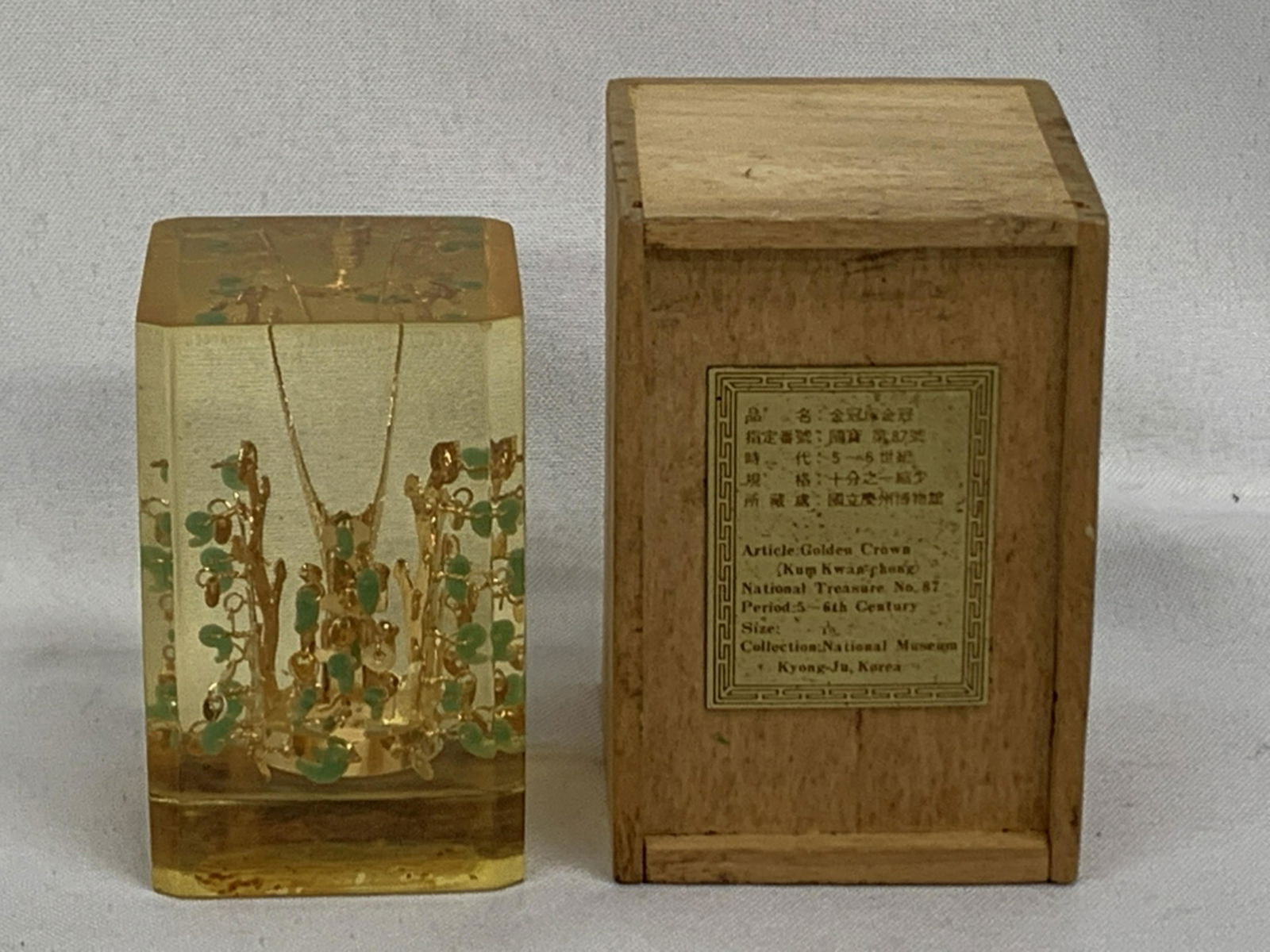 KOREAN NATIONAL MUSEUM TREASURE REPLICA IN LUCITE: Korean National Museum Treasure Kumkwan-Chong No.87 Gold Plated Crown In LuciteGold-colored crown with jade-colored ornaments set in a 4 x 2 x 2 inch plastic block. The plate reads: 'Korean Gold Crown