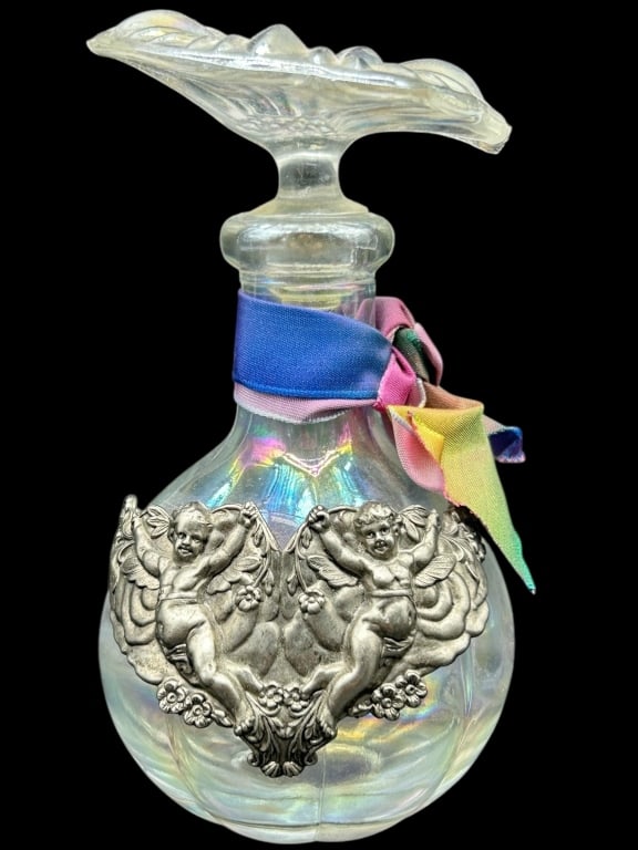 IRIDESCENT GLASS PERFUME BOTTLE 6": - A CHARMING IRIDESCENT GLASS PERFUME BOTTLE FEATURING A SCALLOPED STOPPER AND ORNATE EMBOSSED METAL OVERLAY WITH TWO CHERUBS FRAMING A CENTRAL HEART MOTIF. ADORNED WITH A MULTI-COLOR RIBBON AT THE NE