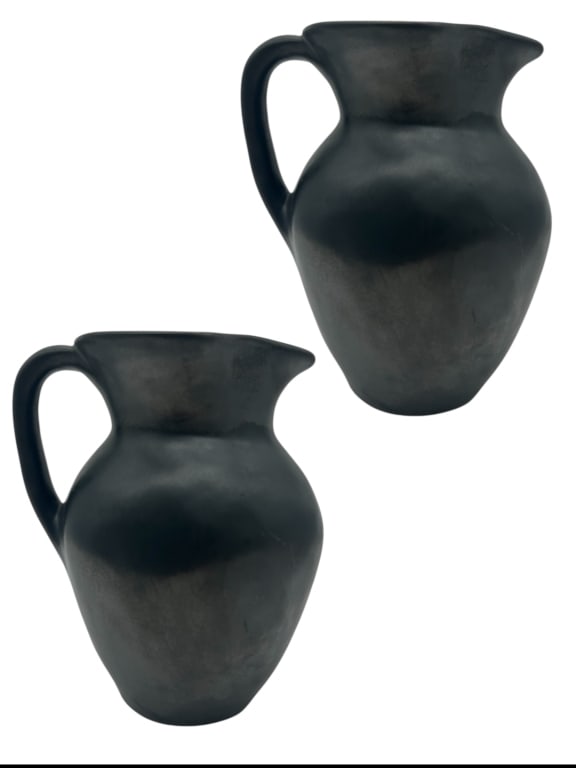 PAIR OF BLACKWARE POTTERY PITCHERS 8.5": - A STRIKING SET OF TWO HAND-CRAFTED BLACK CLAY PITCHERS, FEATURING A CLASSIC CURVED FORM WITH A SINGLE HANDLE AND POUR SPOUT. THEIR MATTE CHARCOAL FINISH RESEMBLES SOUTHWESTERN OR PUEBLO-STYLE BLACKW