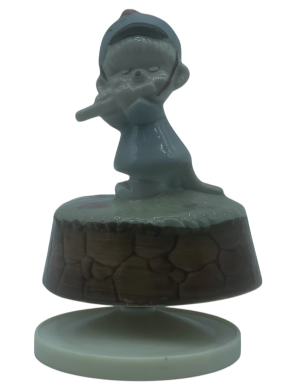 VINTAGE PORCELAIN MUSIC BOX FIGURINE, 5": VINTAGE PORCELAIN MUSIC BOX FIGURINE - GOOD PRE-OWNED CONDITION - 5" H X 3.5" W APPROX - FEATURES A YOUNG CHILD IN A BLUE OUTFIT PLAYING A FLUTE, STANDING ON A STONE WALL-THEMED BASE. HAND-PAINTED GLA