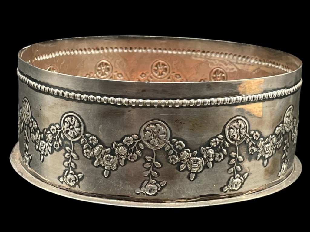 ANTIQUE STERLING SILVER WINE BOTTLE COASTER 104.5G: ANTIQUE STERLING SILVER WINE BOTTLE COASTER WITH A REPOUSSÉ GARLAND AND MEDALLION DESIGN 104.5G -VERY GOOD PRE OWNED CONDITION -APPROX 1.75" X 5" -DECORATED WITH DRAPED FLORAL SWAGS CONNECTED BY CIRC