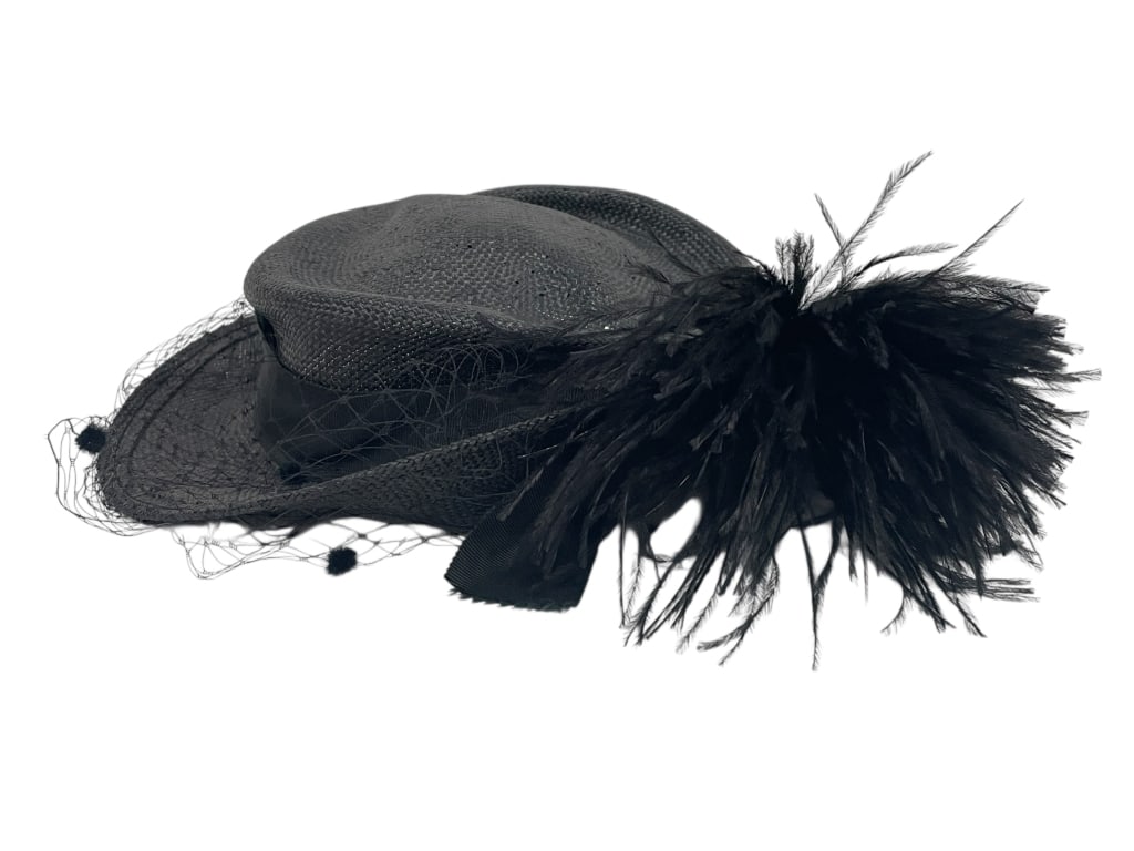 FEDORIA VINTAGE BLACK FEATHERED MILLINERY HAT: FEDORIA VINTAGE BLACK FEATHERED MILLINERY HAT WITH VEIL NETTING -Vintage condition -Inside diameter approx 7" -Elegant vintage black hat featuring a woven straw base accented with a dramatic feather p