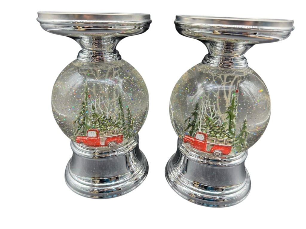 PAIR OF CHRISTMAS SNOW GLOBE CANDLE PEDESTALS: This festive pair of holiday candle pedestals each features a water-filled glitter snow globe base with a red truck carrying a Christmas tree, topped with a silver-tone candle plate. Measuring approxi