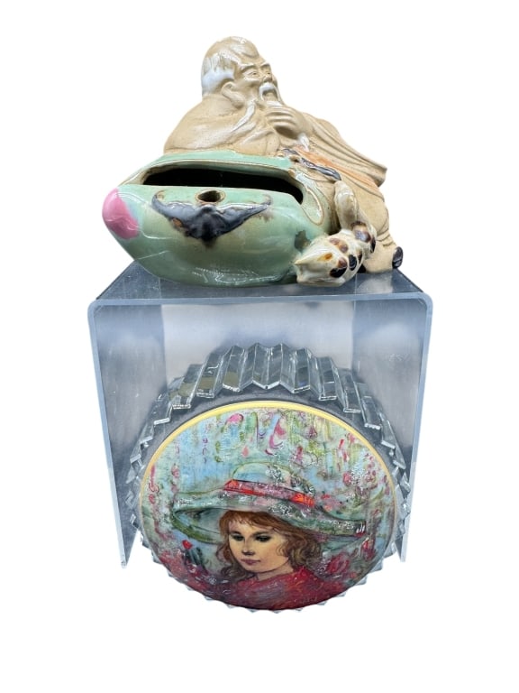 LOT OF A VTG MUD MAN & EDNA HIBEL PAPERWEIGHT: This lot features a vintage Chinese ceramic reclining sage Mud Man incense holder in earth-tone and celadon glazes along with a round Edna Hibel hand-painted paperweight depicting a young girl in a bo