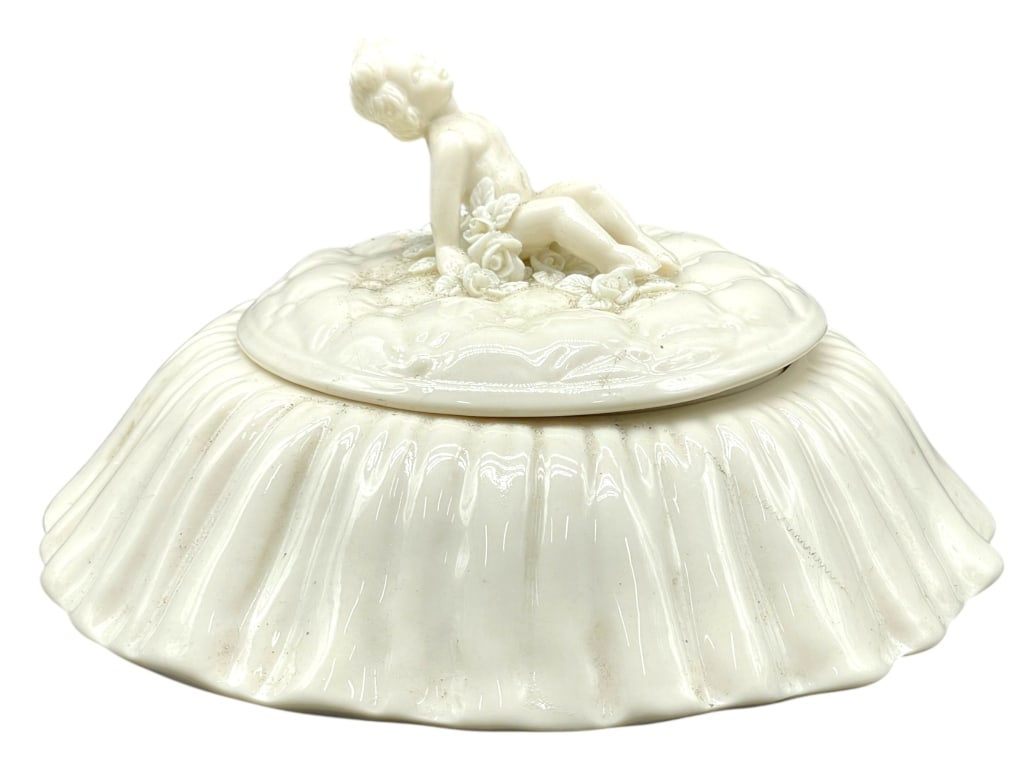 DOROTHY OKUMOTO PORCELAIN LIDDED DISH W CHERUB 6": DOROTHY OKUMOTO PORCELAIN SCULPTURAL LIDDED DISH -Handcrafted studio porcelain lidded bowl featuring a sculptural reclining figure atop the lid, executed in a soft ivory glaze with subtle ribbed detai