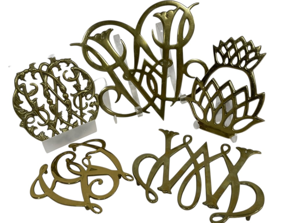 DECORATIVE BRASS MONOGRAM & SCROLLWORK TRIVETS: DECORATIVE BRASS MONOGRAM & SCROLLWORK TRIVETS – -Decorative lot of vintage brass trivets featuring openwork monogram letters, scrolling forms, and stylized floral and geometric motifs, all finished