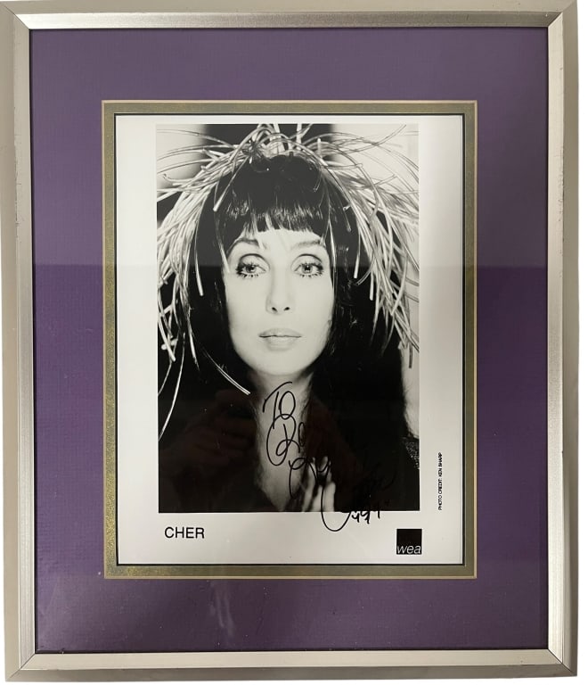 "Goddess of Pop," Cher hand-signed: This framed photograph features an original hand-signed promotional portrait of the "Goddess of Pop," Cher. Item Identification Subject: The photograph is a promotional headshot for Cher's multi-plati