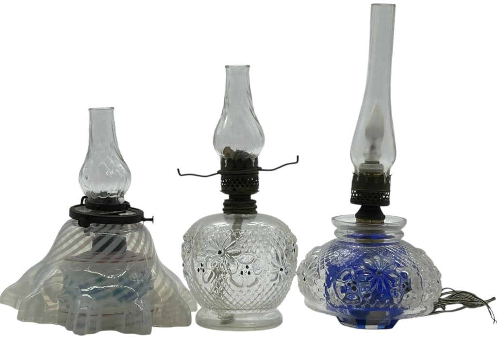 LOT OF 3 VINTAGE GLASS CLEAR & COBALT OIL LAMPS 9": Charming lot of three vintage oil lamps featuring pressed and molded glass fonts in clear and cobalt blue, each fitted with metal burners and glass chimneys. Designs include floral and geometric embos
