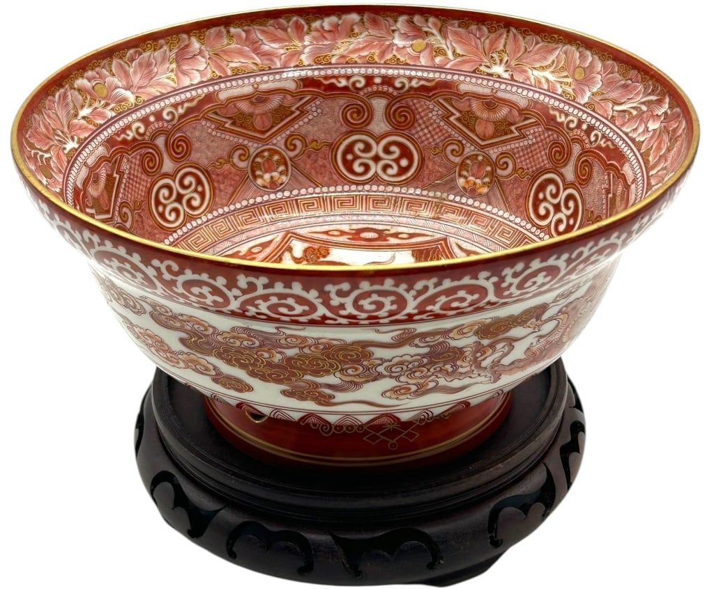 LARGE ORIENTAL PORCELAIN BOWL WITH WOOD STAND: LARGE ORIENTAL STYLE RED & WHITE PORCELAIN FOOTED BOWL WITH CARVED WOOD STAND Striking large decorative porcelain bowl featuring an intricate red and white motif with gilt accents, showcasing traditio