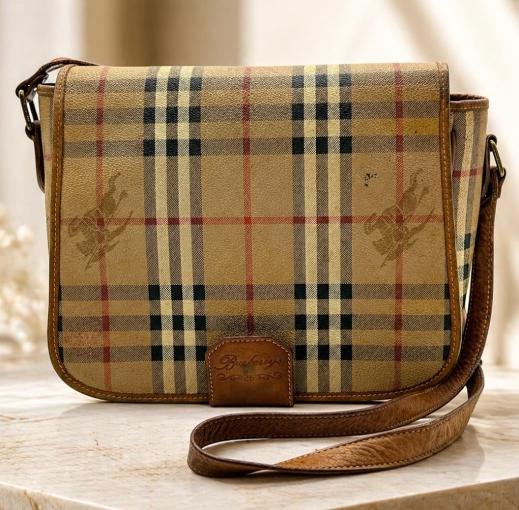 VINTAGE BURBERRYS NOVA CHECK BAG CROSSBODY BAG: Vintage Burberrys crossbody shoulder bag featuring the classic tan Nova Check plaid coated canvas exterior with black, cream, and red striping, brown leather trim, flap front, adjustable leather shoul