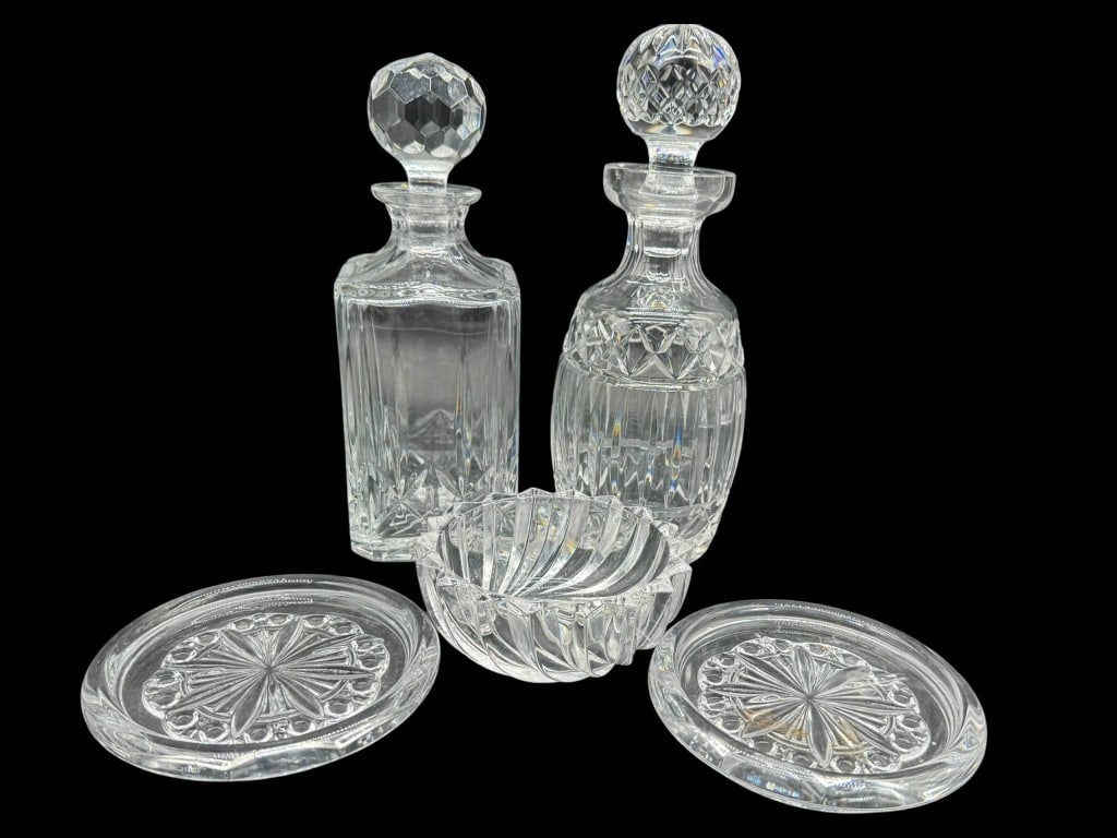 CUT GLASS DECANTERS AND COASTERS SET: Two cut glass decanters with stoppers, two round cut glass coasters, and one cut glass bowl. Height of the decanters is approximately 10 inches. Shipping Available at www.DeJaVuAuctionShipping.com By 