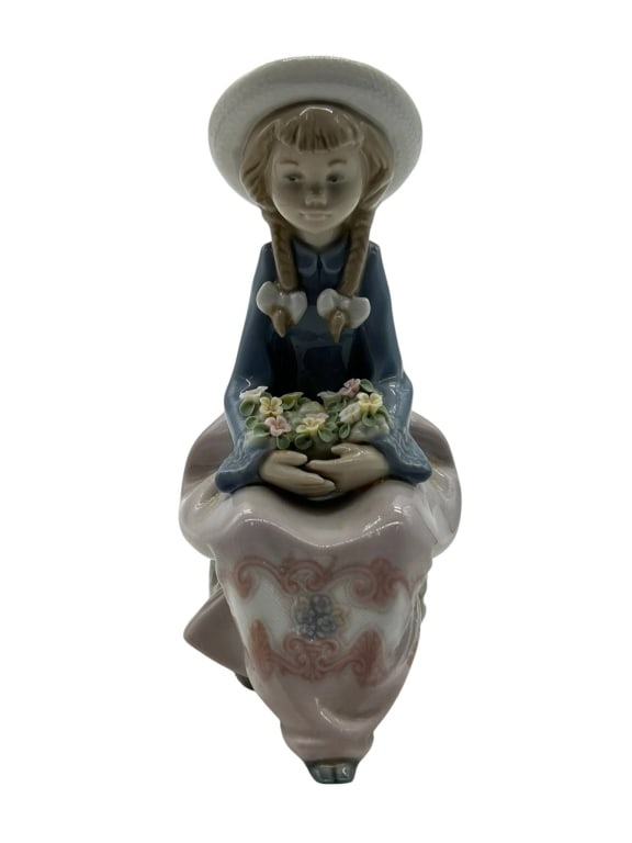 LLADRO GIRL WITH FLOWERS FIGURINE #5554 6": Lladro porcelain figurine depicting a seated young girl in a wide-brimmed hat with braided hair, holding a basket filled with delicate applied flowers. This charming Spanish porcelain figure features 