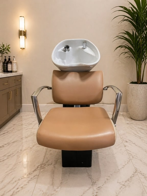 MODERN SALON SHAMPOO CHAIR WITH CERAMIC SINK: This professional-grade salon shampoo chair features a sleek, contemporary design combining comfort and functionality. Upholstered in a warm caramel-tone vinyl, the chair offers a padded seat and ergo