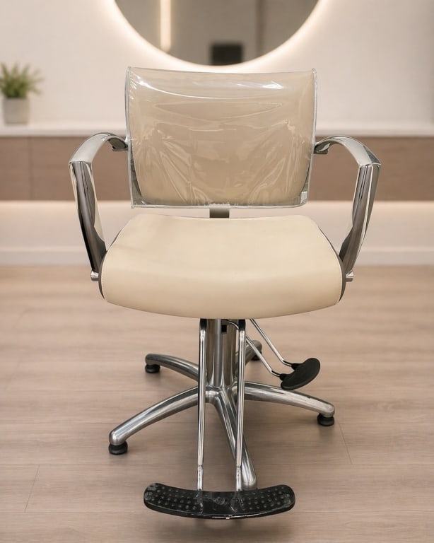 MODERN SALON STYLING CHAIR WITH CHROME BASE: This contemporary salon styling chair features a sleek, professional design ideal for hair salons, barber shops, or spa environments. Upholstered in a neutral cream-tone vinyl with a protective clear 