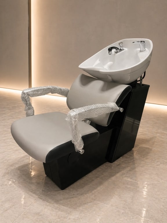 MODERN PROFESSIONAL SALON BACKWASH CHAIR: Contemporary salon shampoo backwash chair featuring a padded upholstered seat and backrest in a light neutral tone with contrasting dark base, integrated white ceramic shampoo bowl, and chrome faucet 