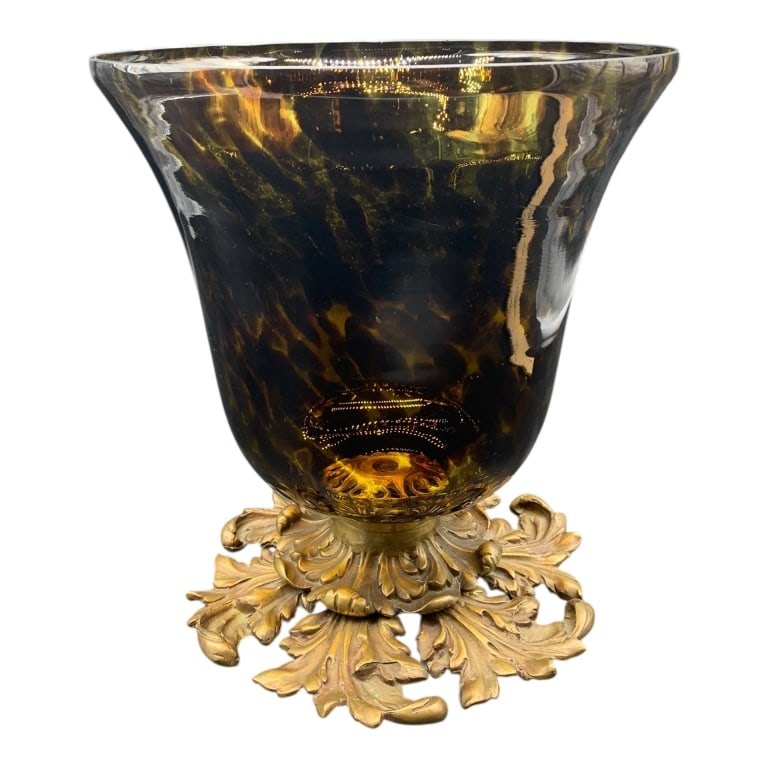 TORTOISESHELL PATTERN ART GLASS VASE WITH GILT FLO: Glass vase featuring a flared form with mottled amber coloring, supported by an ornate brass or gilt metal leaf-motif base. Includes protective pads on the underside. Approximately 12 inches tall, app