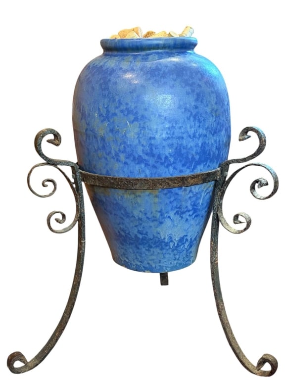 LARGE BLUE CERAMIC URN WITH IRON STAND 25": Striking large blue ceramic urn, approximately 25 inches tall including ornate black wrought iron scroll stand. Features a vivid mottled blue glaze and wide mouth, currently filled with wine corks. Ex