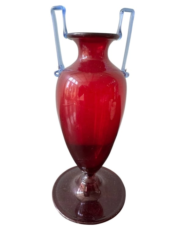 RUBY RED GLASS VASE WITH BLUE HANDLES: Elegant ruby red glass vase featuring distinctive blue glass handles and a flared rim. Stands approximately 10 inches tall with a classic amphora-inspired silhouette. A striking decorative piece for a
