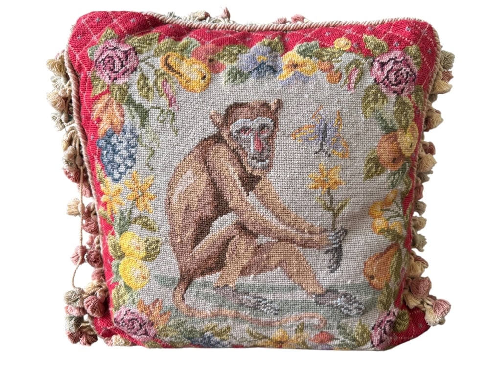 NEEDLEPOINT PILLOW WITH MONKEY DESIGN: Handcrafted needlepoint pillow measuring approximately 17 x 16 inches. Features a central monkey motif surrounded by colorful fruit and floral border, with decorative fringe. Vintage charm and detaile