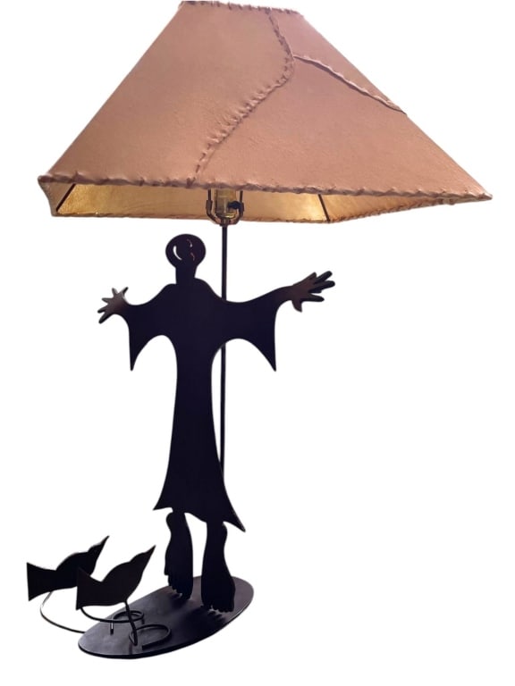 HANDCRAFTED METAL LAMP WITH FIGURE AND BIRD 33": Unique table lamp with a handcrafted metal base depicting a stylized figure and two birds. The lamp features a stitched parchment shade. Ideal for eclectic or modern decor. Height shown with tape meas