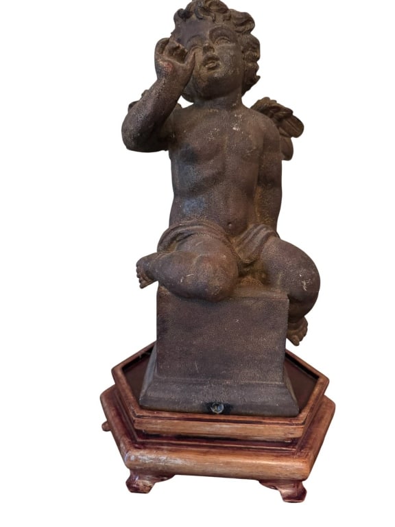 WINGED BRONZE TONE CHERUB FIGURINE ON WOOD BASE: Bronze tone composite cherub figurine with detailed wings, seated on a square block, mounted on a hexagonal wood plinth. Figurine features classic cherub styling with expressive pose. Shows patina fro
