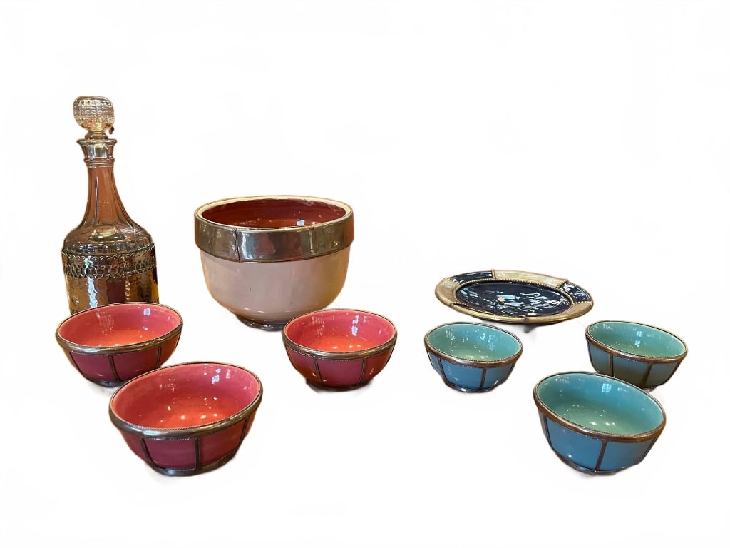 VINTAGE CERAMIC AND GLASS TABLEWARE SET: This eclectic set includes a glass decanter with etched metal overlay (approx. 11" tall), ceramic punch bowl with metallic rim, four red and two blue ceramic bowls with metal trim, and a decorative