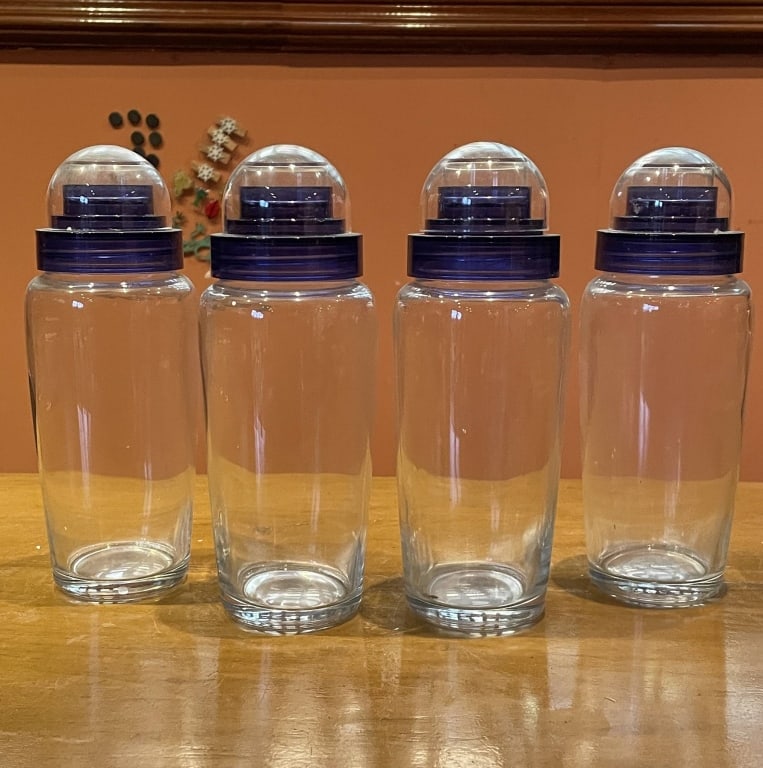 4 COBALT ACCENT GLASS APOTHECARY STORAGE JARS 9": Four clear glass storage jars, each with a domed purple plastic lid. Approximate height is 9" and diameter is 3". Ideal for kitchen storage or decorative use.