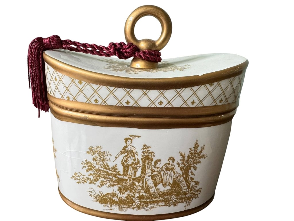 SEDA FRANCE TOILE PIG CANDLE WITH LID: Decorative Seda France porcelain candle with a gold-tone handle and toile design. Features a red tassel and a Barnier Quince scent. The reusable container adds elegance to any space. Includes