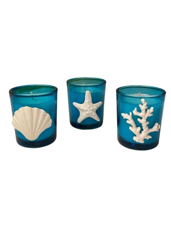 THREE COASTAL OCEAN THEME BLUE GLASS CANDLES 3.25": Three blue glass candles, each featuring a white ocean-themed ornament: a seashell, a starfish, and a coral. Each candle measures approximately 3.25 inches tall. Great coastal decor accent for home or