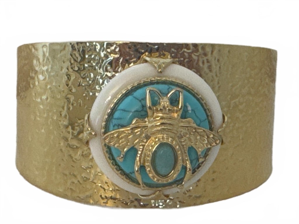 GOLD TONE CUFF WITH TURQUOISE BEE MOTIF: Textured gold tone cuff bracelet features a prominent bee motif over a turquoise center medallion with white accent ring. Eye-catching, nature-inspired design, suitable as a statement accessory. Measu