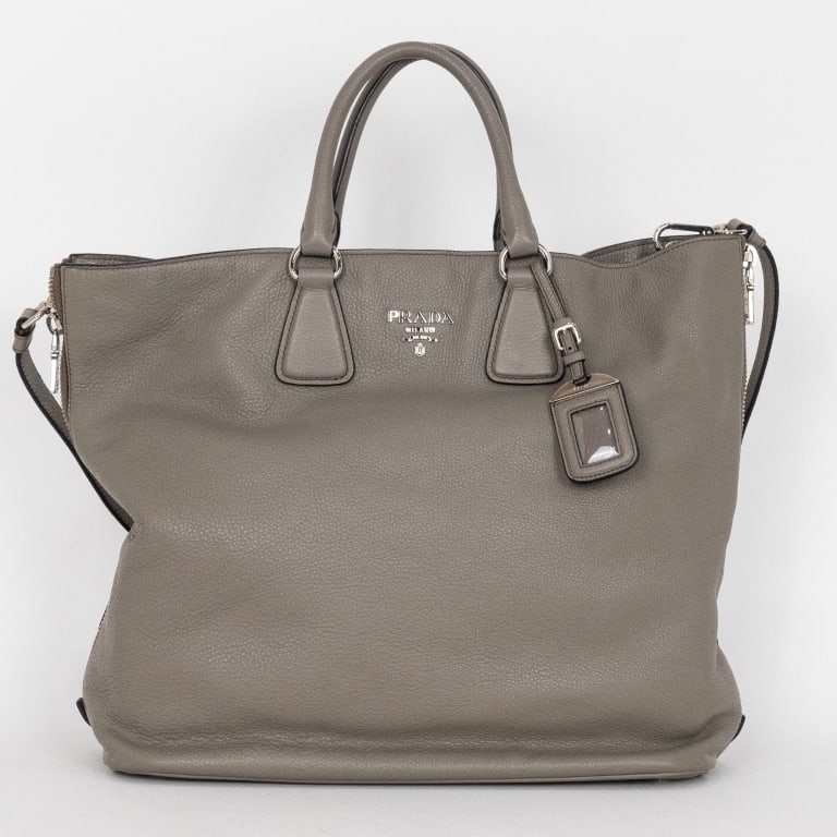 PRADA LARGE GREY VITELLO DAINO TOTE BAG: The Prada Classic Large Shopping Tote is crafted in luxurious grey Vitello Daino leather and accented with sleek silver-tone hardware. Known for its supple grained texture and exceptional durability, 