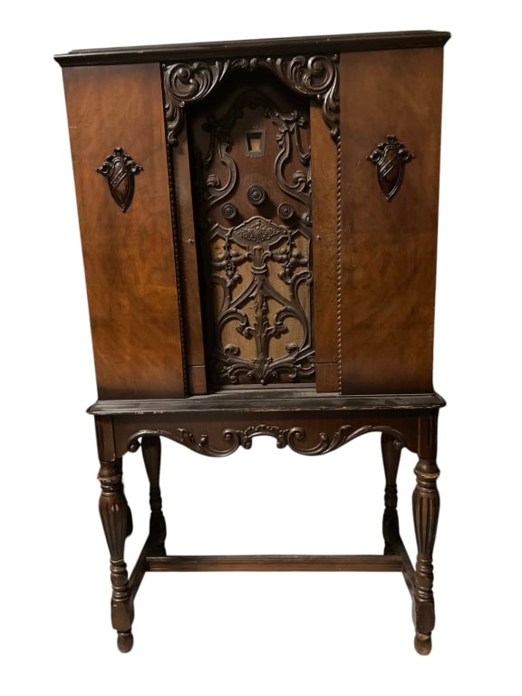 ANTIQUE FRENCH PROVINCIAL RADIO CABINET ON STAND: Vintage French Provincial Style Cabinet on StandElegant cabinet featuring a shaped crest with carved scrollwork, arched double doors, and warm figured wood veneer. Raised on turned legs with a decorat