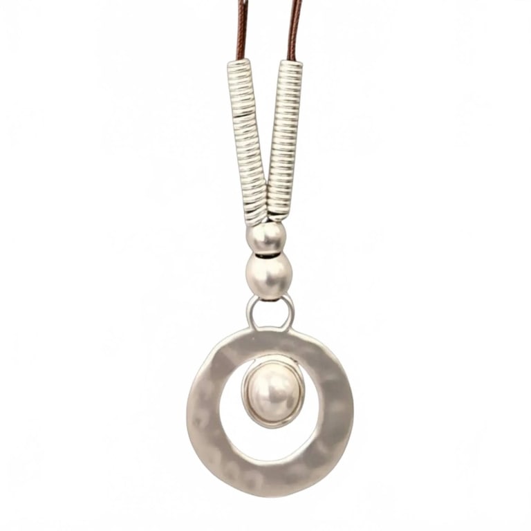 Chunky Boho Western Pearl Pendant Necklace: This statement necklace features a large circular hammered silver-toned pendant with a raised center orb, accented by coiled silver elements and a brown cord. Bold, contemporary design ideal for addin