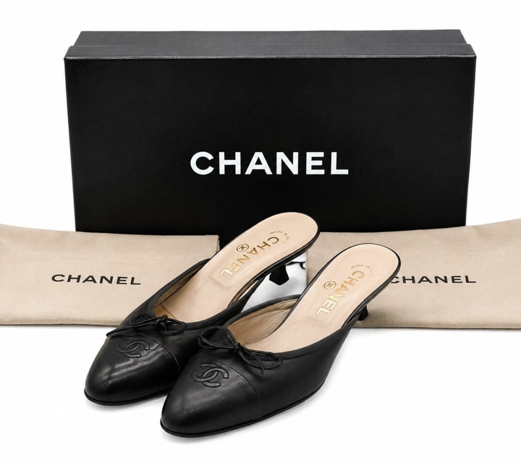 CHANEL CC LEATHER PATENT MULES 37.5: Elegant Chanel slip-on mules crafted in smooth black leather with glossy patent leather cap toes featuring the iconic embroidered interlocking CC logo. The shoes are accented with delicate leather bow