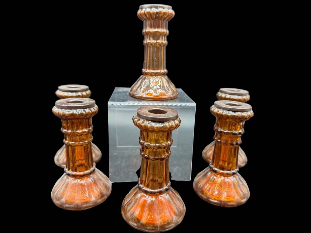 6 AMBER GLASS CANDLE HOLDERS: 6 candle holders made from amber-colored glass. Each holder features a flared base and ribbed column design. The height of one holder is approximately 7 inches. Shipping Available at www.DeJaVuAuction