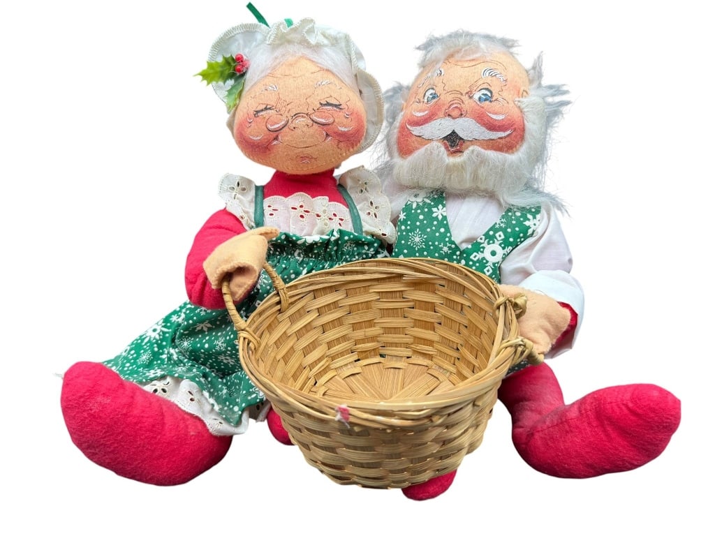 ANNALEE MR. AND MRS. CLAUS PLUSH DOLLS: Plush Mr. and Mrs. Claus dolls dressed in holiday attire, accompanied by a woven basket. Mr. and Mrs. Claus feature fabric faces, yarn hair, and green-themed costumes with red accents. Shipping Availa