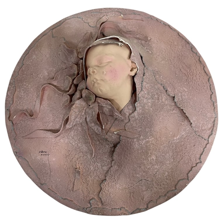 RELIEF SCULPTURE OF SLEEPING CHILD 18": Mixed-media wall sculpture depicting the serene face of a sleeping child emerging from a textured circular form. Signed lower left. The work features dimensional relief construction with a softly