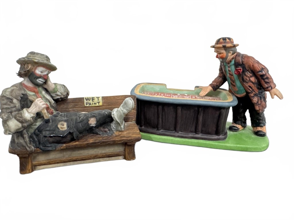Flambro Emmett Kelly Clown Figurines Set: Two Emmett Kelly clown figurines by Flambro. Hand-painted porcelain, depicting comic clown scenes with a craps table and 'Wet Paint' bench. Both figures display original markings on the base. Each mea