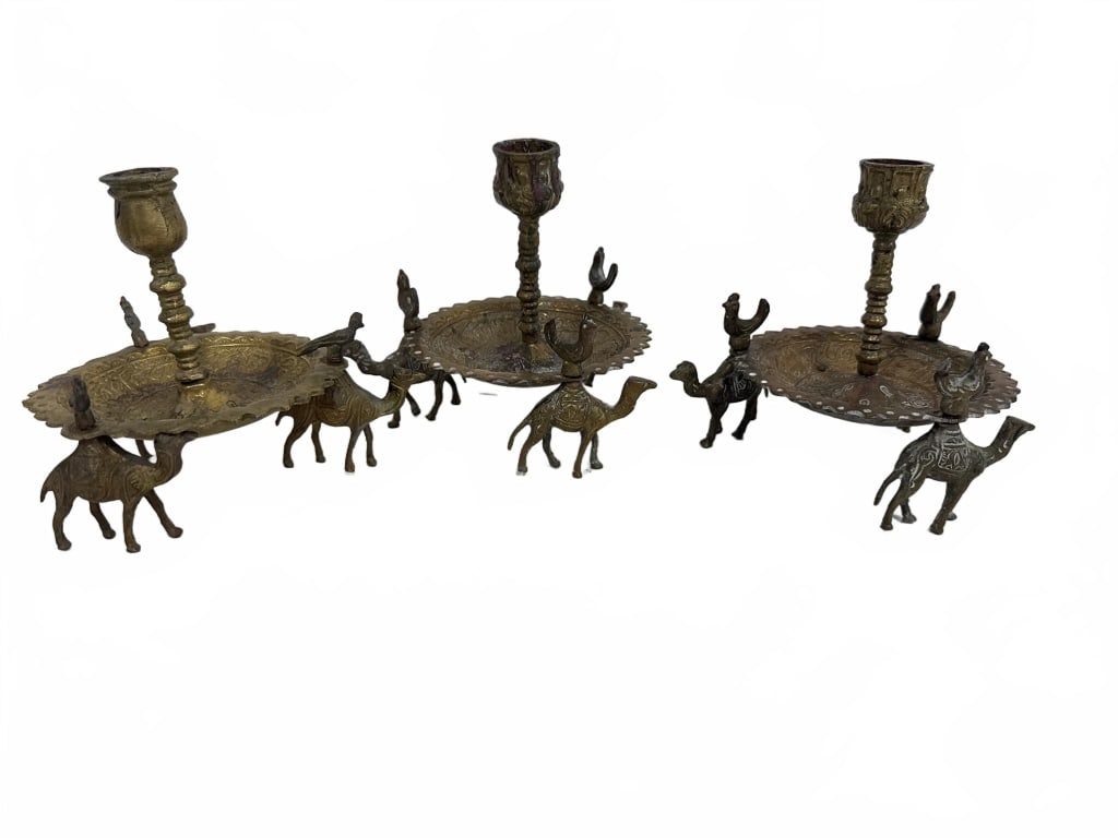 Brass Camel Motif Candle Holders Set of Two: Decorative brass candle holders, each featuring a scalloped circular platform supported by three camel figurines. Vintage patina with intricate detailing. Approximate height is 3.5 inches. Great for e
