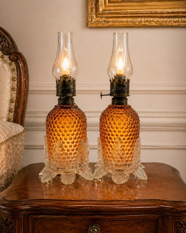 2 HOBNAIL GLASS KEROSENE STYLE ELECTRIC LAMPS 10": Attractive pair of vintage kerosene style electric table lamps featuring amber hobnail glass bodies, clear pressed glass floral/petal form bases, dark metal burner-style collars, clear glass chimney s